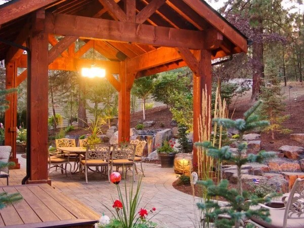 A beautifully designed pergola with a dining table and chairs, surrounded by lush landscaping.